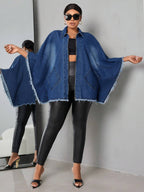 Woman wearing a blue denim cape over a black outfit against a gray background
