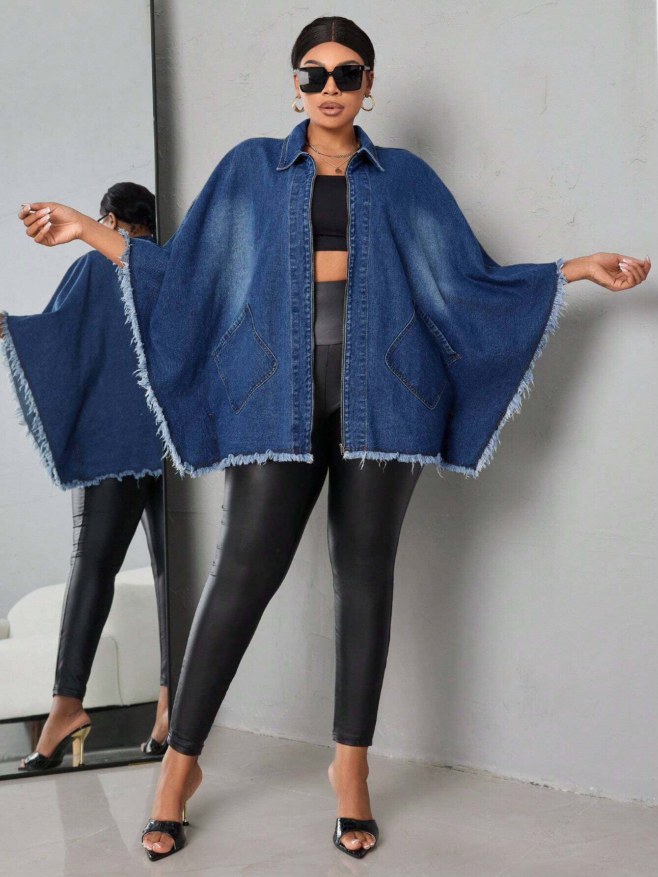 Woman wearing a blue denim cape over a black outfit against a gray background