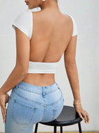 Person wearing a white open-back top and blue jeans sitting on a chair.