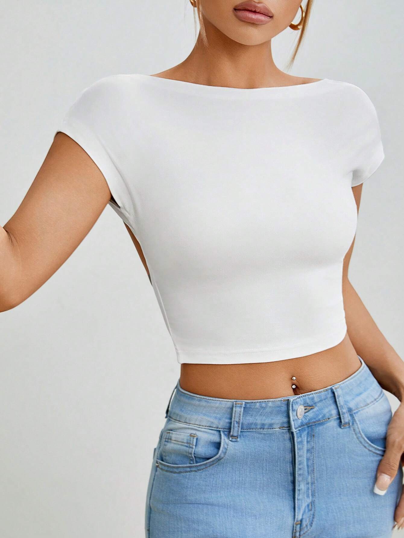 Person wearing a white crop top and blue jeans on a plain background