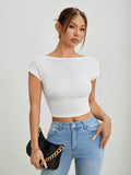 Woman wearing a white crop top and blue jeans, holding a black clutch against a plain background