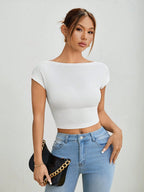 Woman wearing a white crop top and blue jeans, holding a black clutch against a plain background
