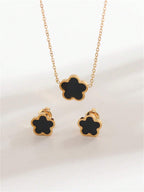 Gold necklace and earrings with black flower-shaped pendants on a light background