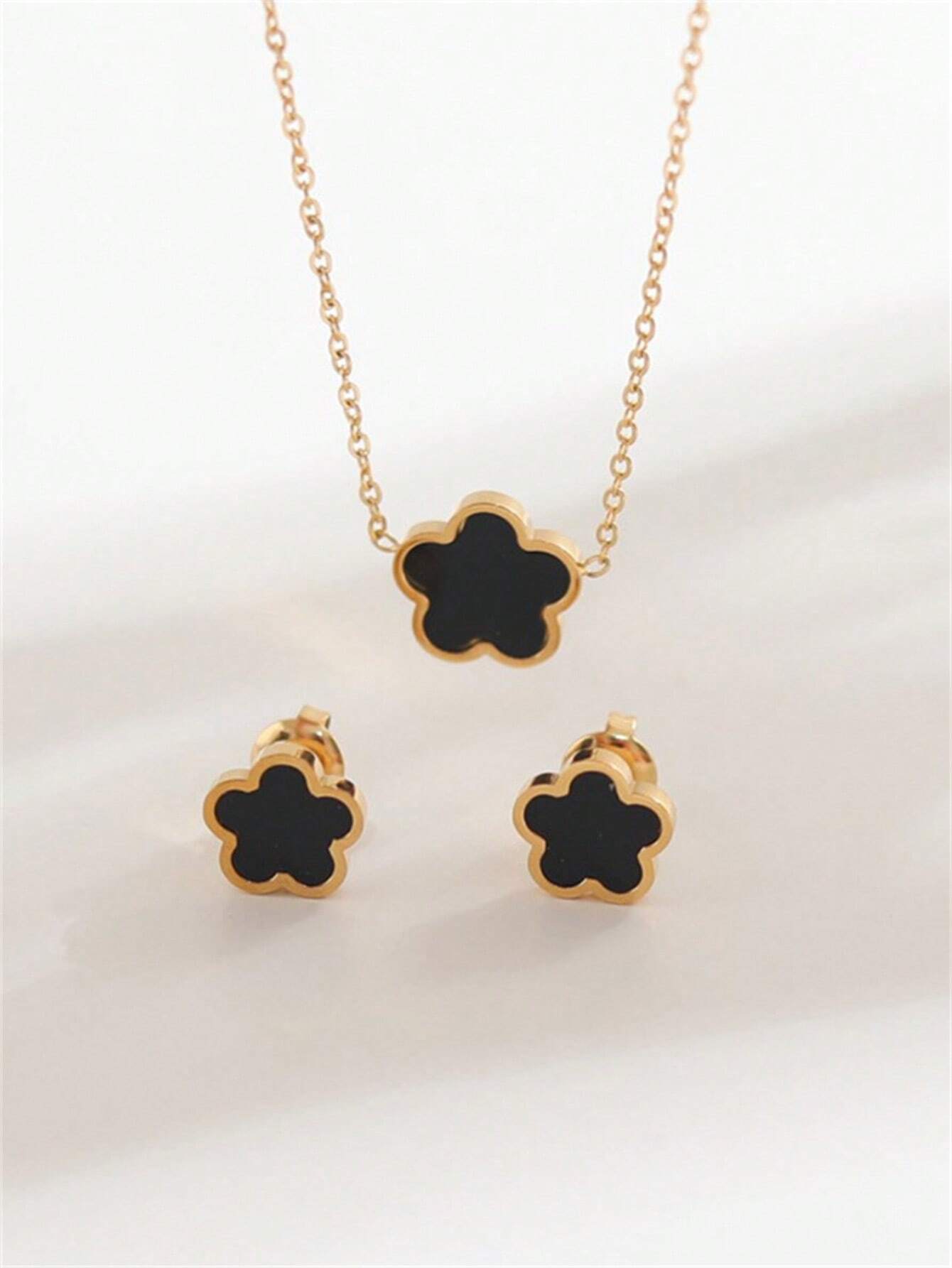 Gold necklace and earrings with black flower-shaped pendants on a light background