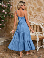 Woman wearing a blue dress standing in front of a stone wall with floral decorations.
