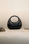 Black handbag with a gold chain on a light surface