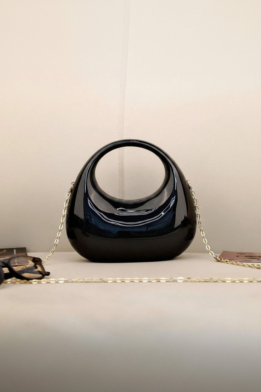 Black handbag with a gold chain on a light surface