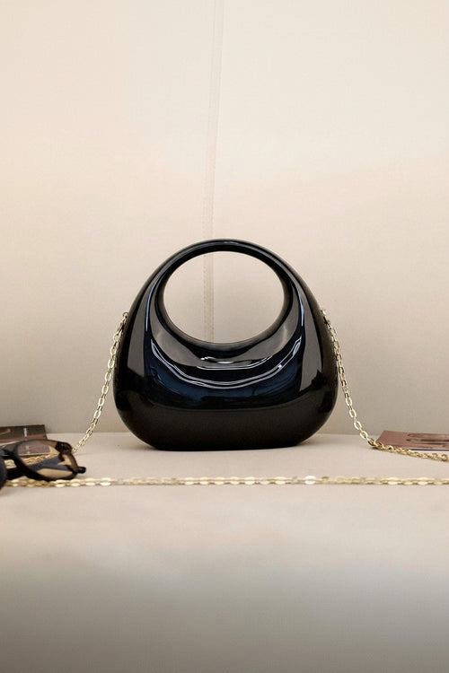 Black handbag with a gold chain on a light surface