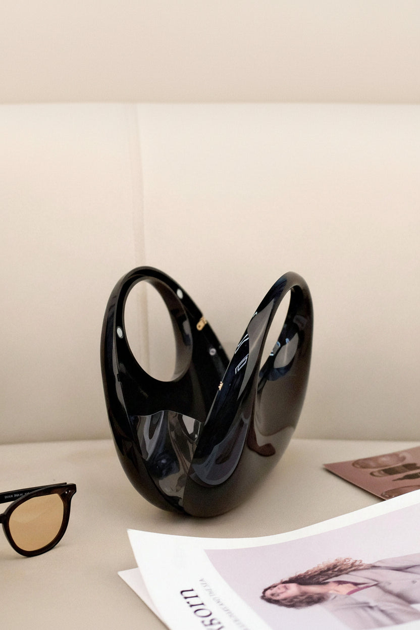 Black vase on a surface with sunglasses and a magazine in the background