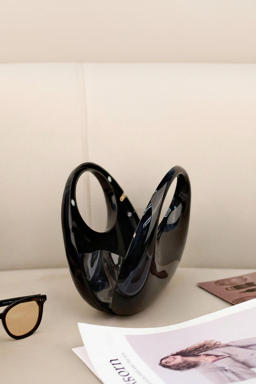 Black vase on a surface with sunglasses and a magazine in the background