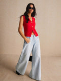 Woman wearing a red sleeveless top and light blue jeans against a beige background