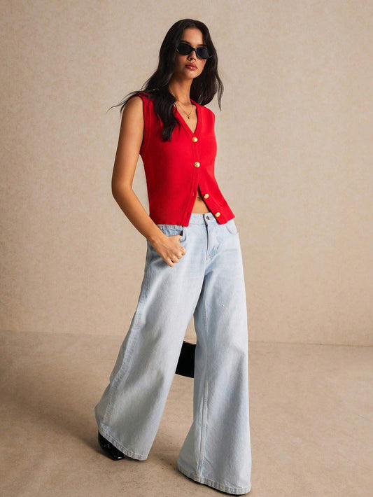 Woman wearing a red sleeveless top and light blue jeans against a beige background
