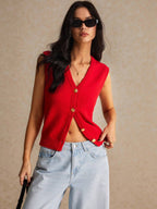 Woman wearing a red sleeveless cardigan and light blue jeans against a beige background