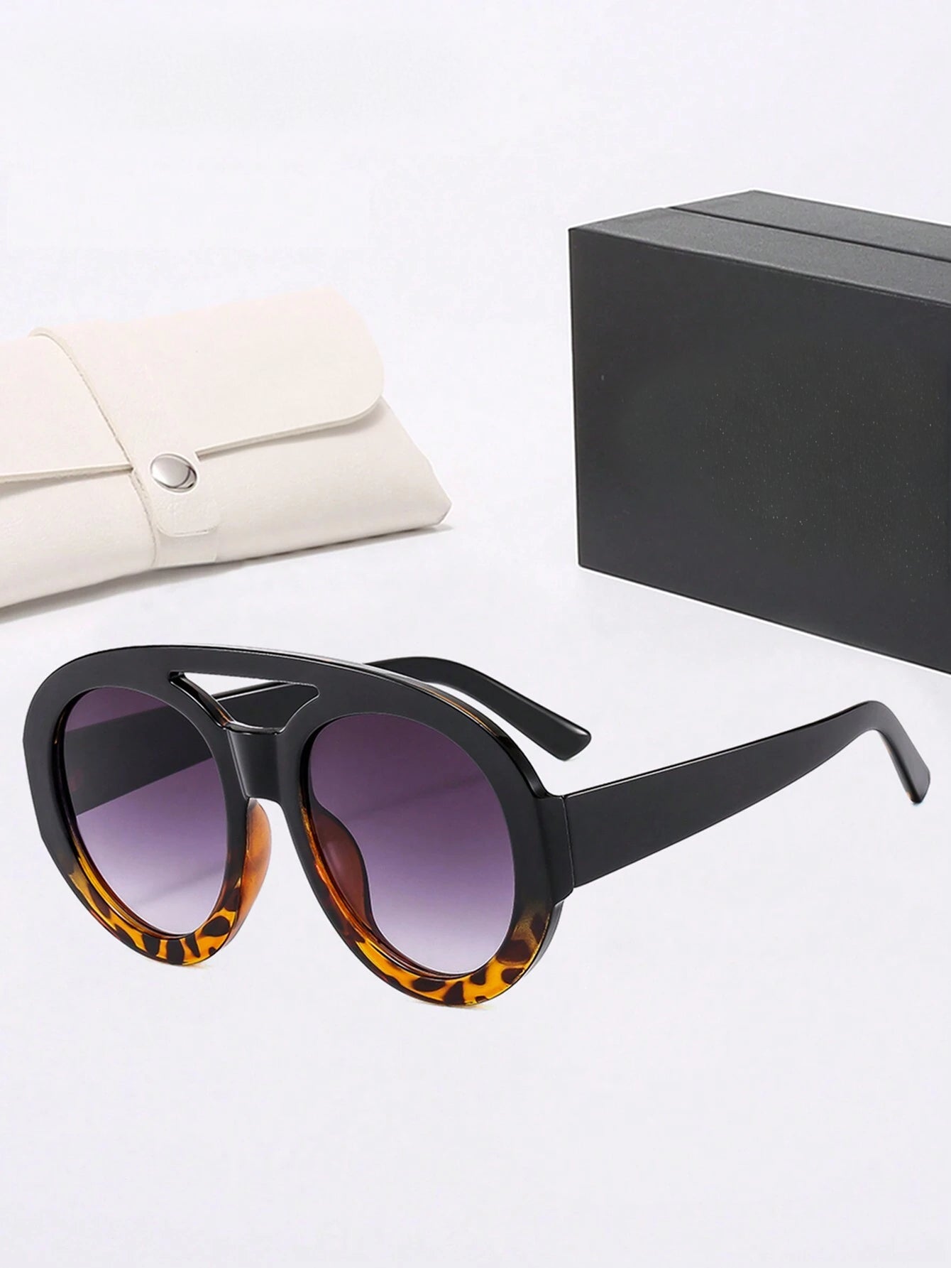 Sunglasses with tortoiseshell frame and purple lenses on a white surface with a black box and beige pouch.