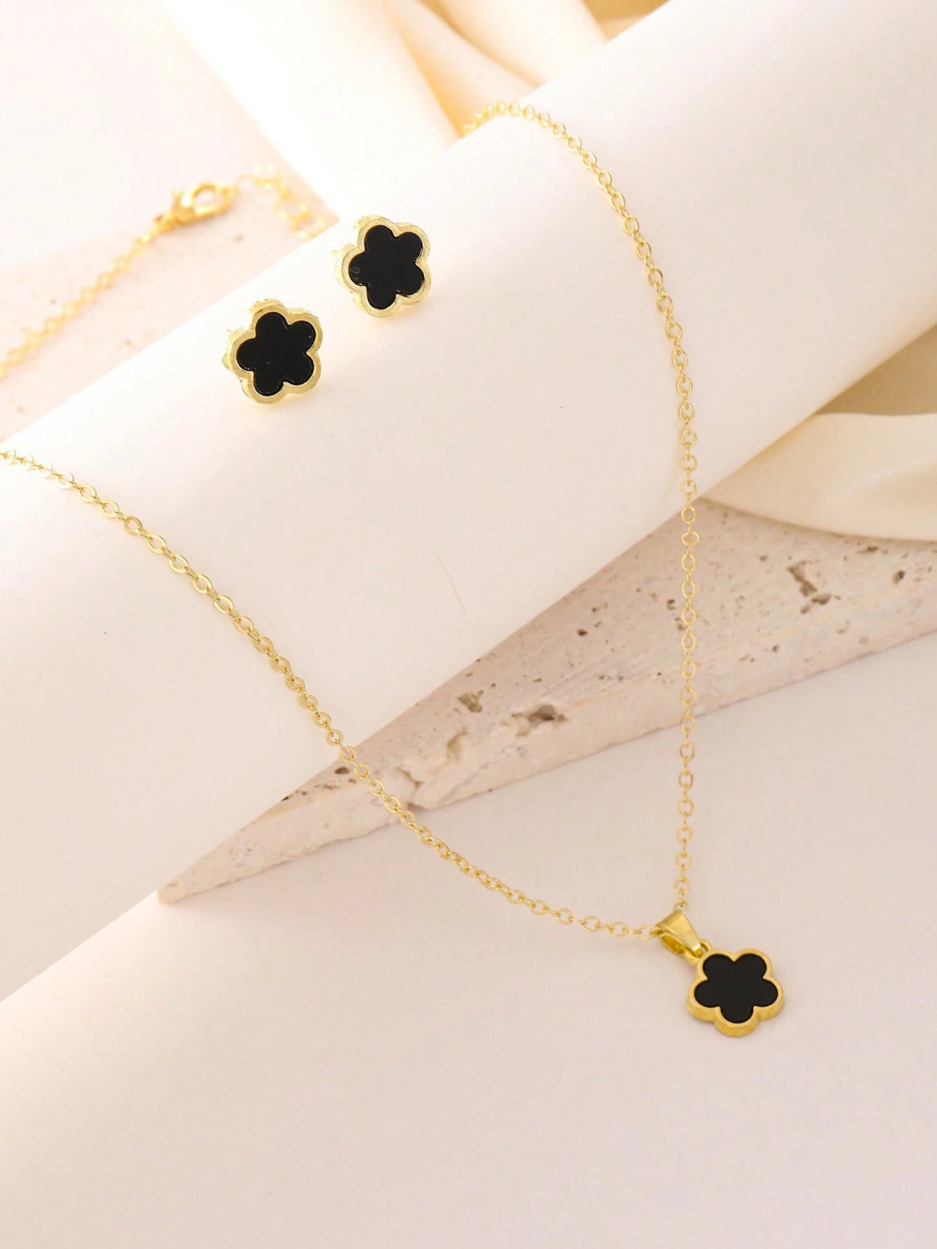 Gold necklace with black clover pendants on a white fabric background