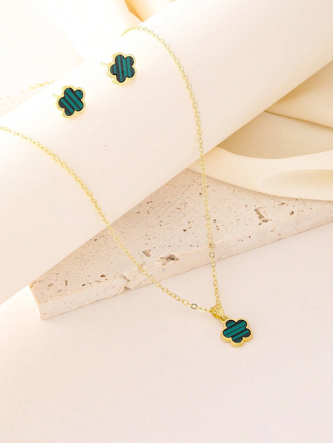 Gold necklace with green clover-shaped pendants on a beige surface