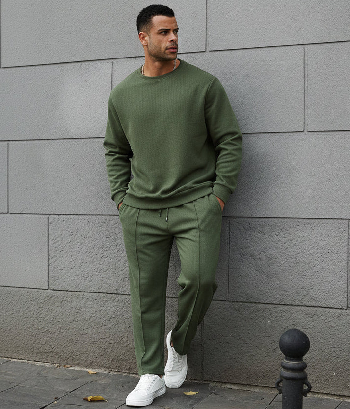 Man wearing a green tracksuit standing against a gray wall.