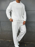 Person wearing a white tracksuit against a gray wall.