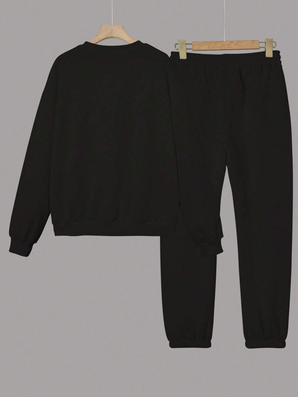 Black sweatshirt and pants set on hangers against a gray background