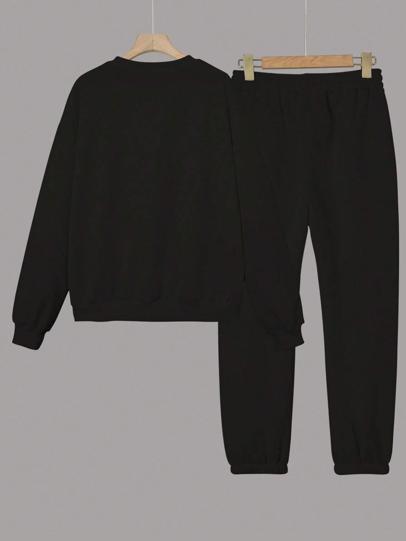 Black sweatshirt and pants set on hangers against a gray background
