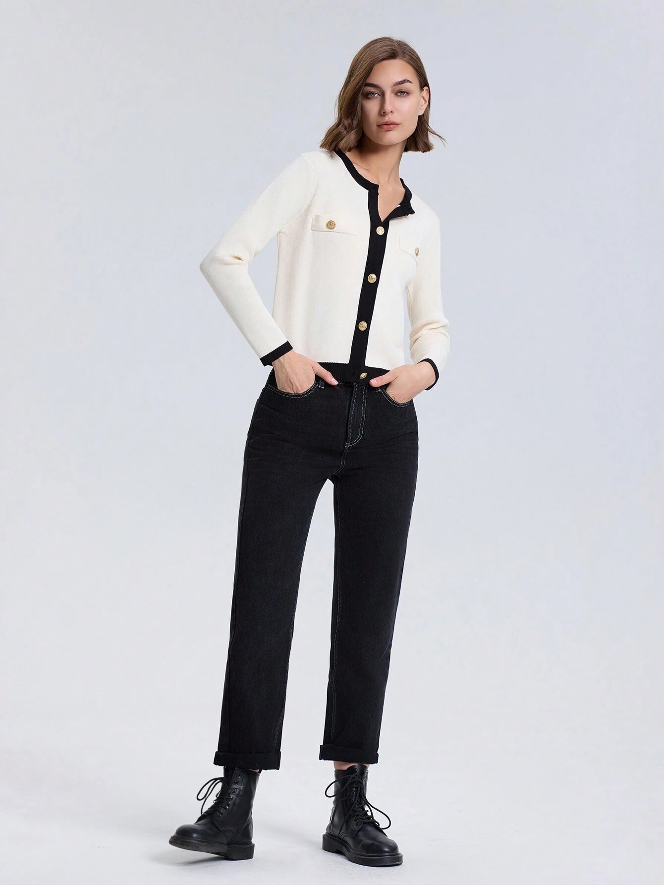 Woman wearing a white jacket with black buttons and black pants on a light gray background
