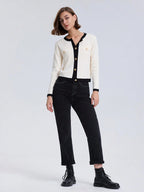 Woman wearing a white cardigan with black trim and black pants on a white background