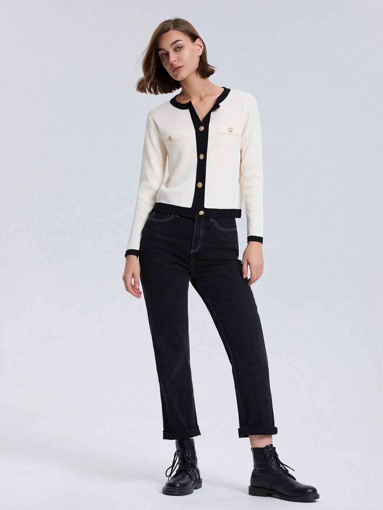 Woman wearing a white cardigan with black trim and black pants on a white background
