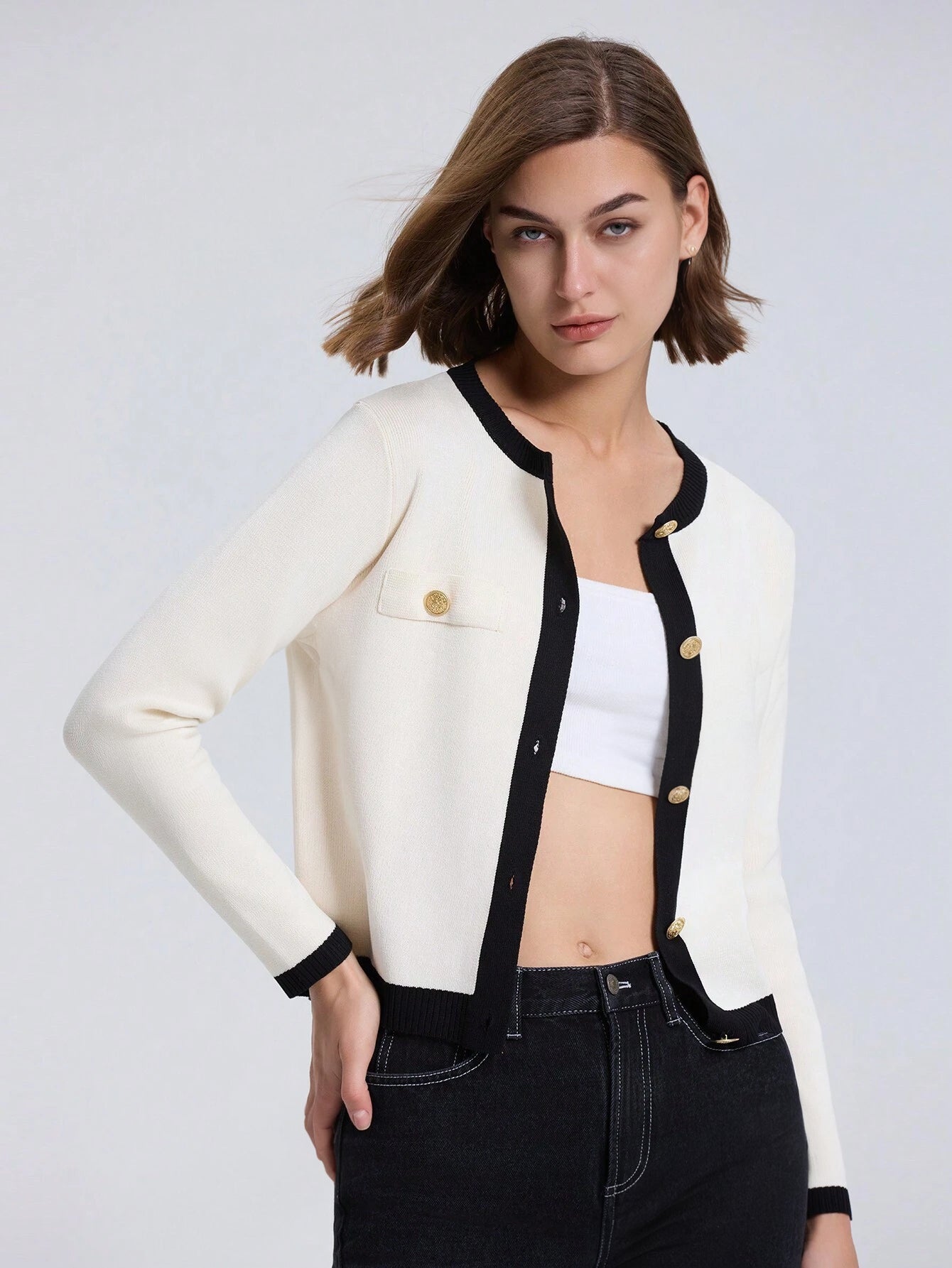 Woman wearing a white cardigan with black trim on a light gray background