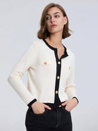 Woman wearing a white and black cardigan with gold buttons on a light gray background