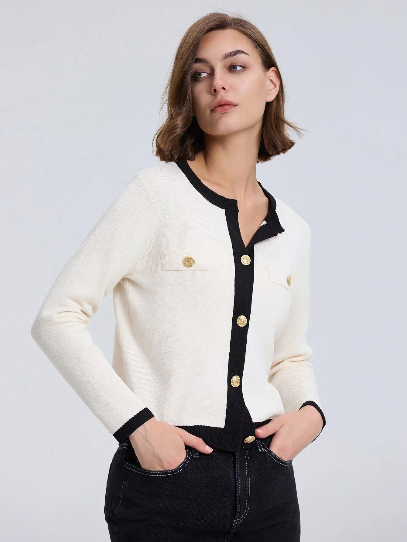 Woman wearing a white and black cardigan with gold buttons on a light gray background