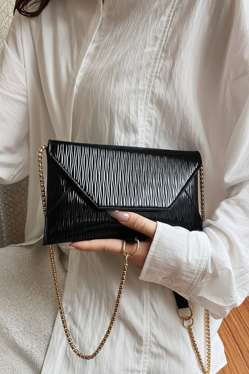 Person holding a black handbag with a chain strap against a neutral background