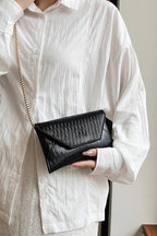 Person holding a black clutch bag with a gold chain strap against a neutral background