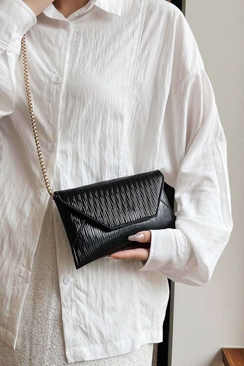 Person holding a black clutch bag with a gold chain strap against a neutral background