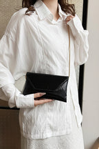 Person wearing a white shirt holding a black clutch with a gold chain.