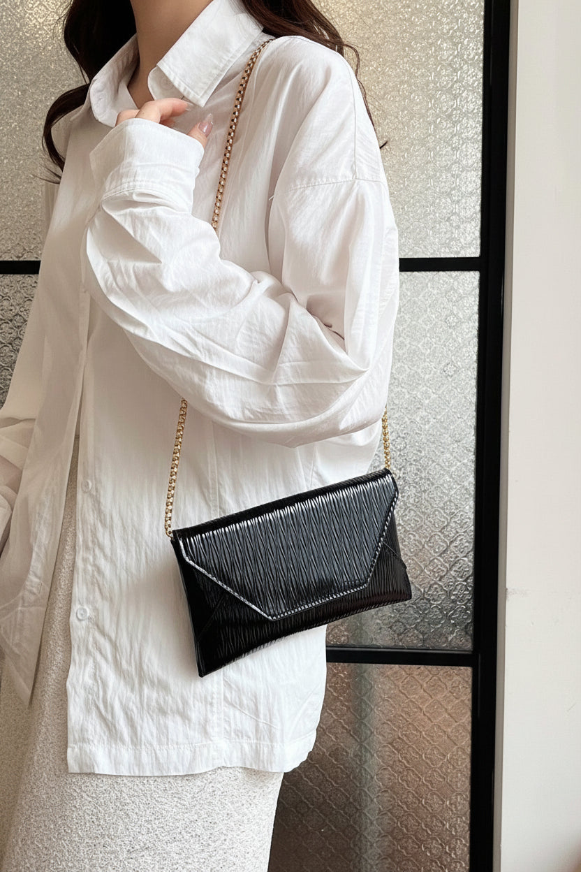 Person wearing a white coat holding a black handbag with a gold chain strap.