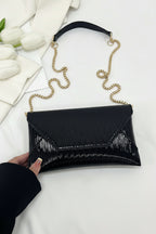 Black clutch with gold chain strap on a white surface with flowers