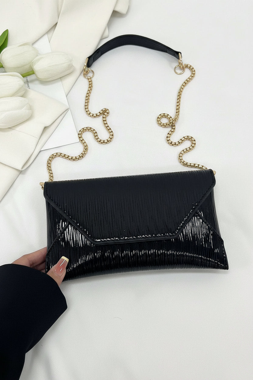 Black clutch with gold chain strap on a white surface with flowers