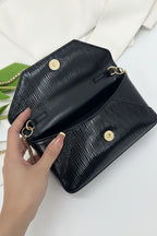 Black handbag with gold chain strap held by a hand on a white background