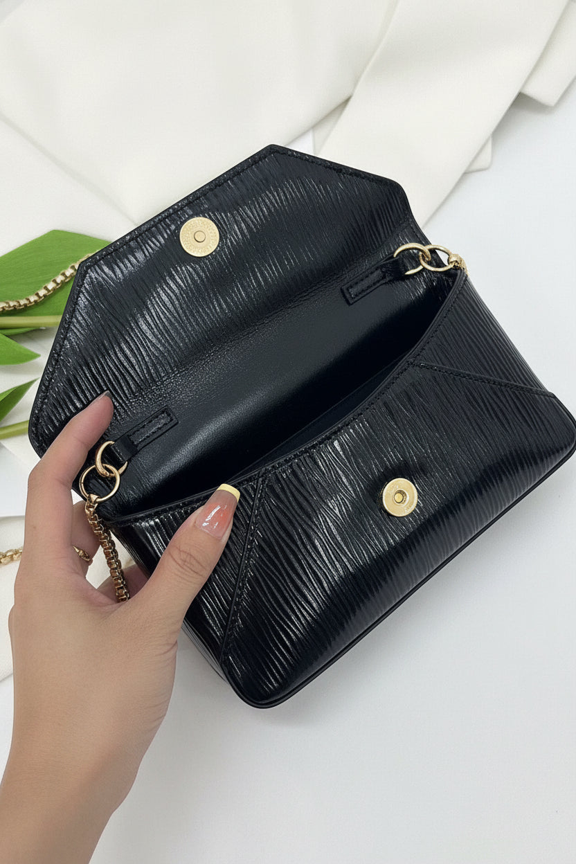 Black handbag with gold chain strap held by a hand on a white background