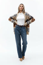 Woman wearing a patterned cardigan with text, white shirt, and blue jeans outdoors.