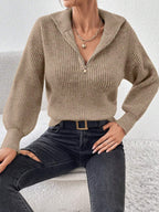 Person wearing a beige knitted sweater and black pants against a white background