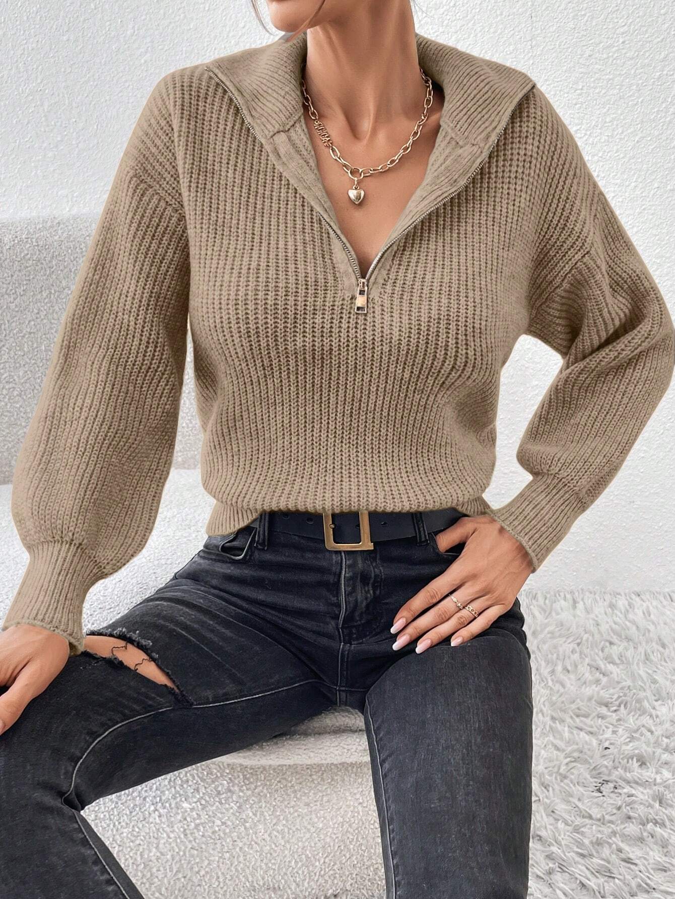 Person wearing a beige knitted sweater and black pants against a white background