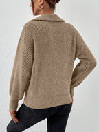 Person wearing a beige knitted sweater and black pants against a white background