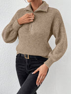 Person wearing a beige knitted sweater and black pants against a white background