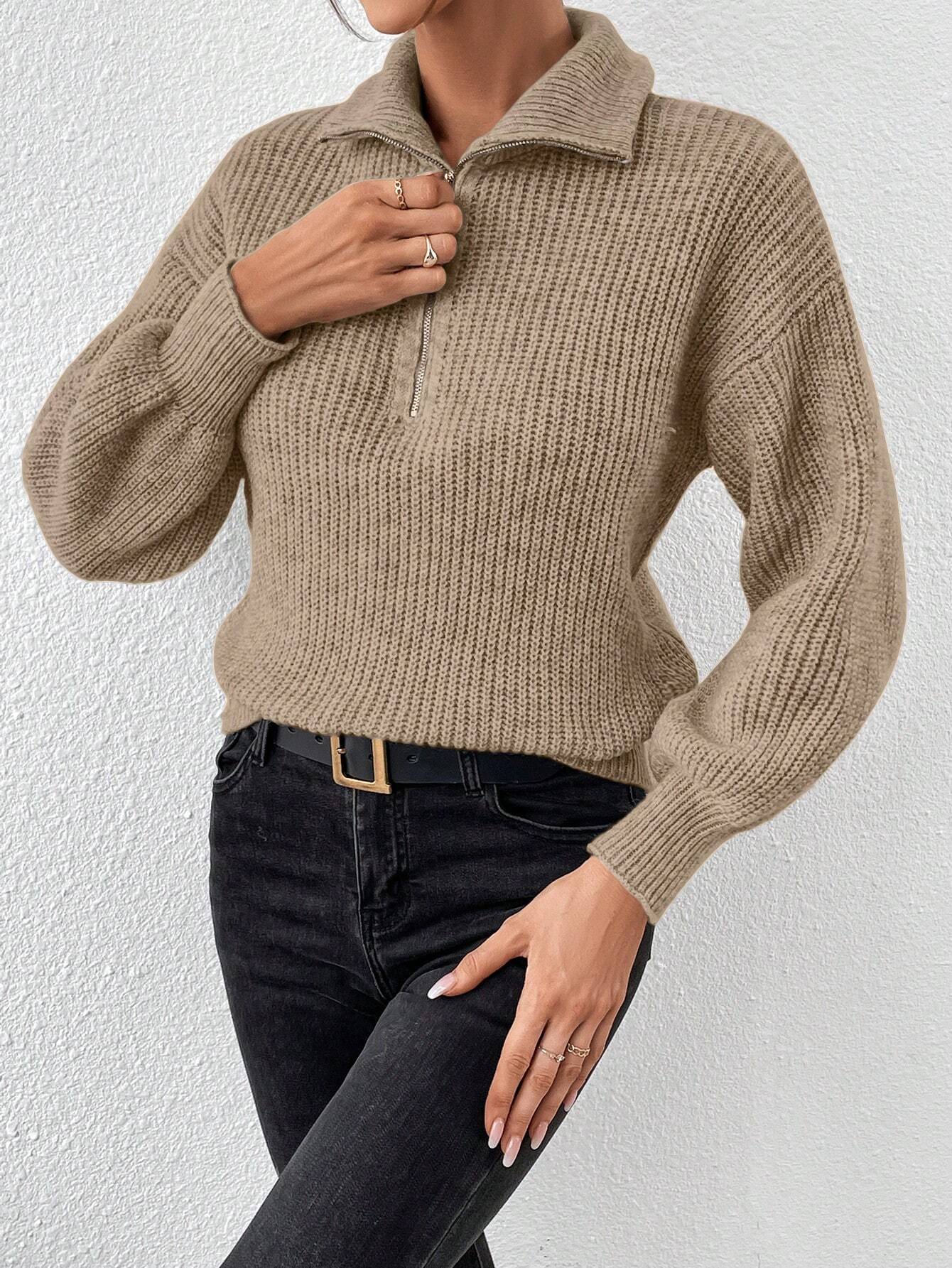 Person wearing a beige knitted sweater and black pants against a white background