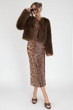 Woman in leopard print dress and brown fur coat standing on a white background.