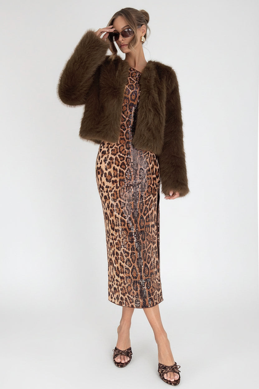 Woman in leopard print dress and brown fur coat standing on a white background.