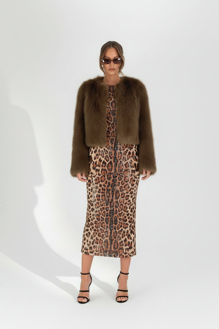 Woman wearing a brown fur coat over a leopard print dress against a white background