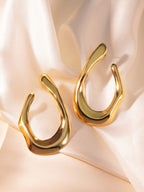 Gold U-shaped earrings on a soft pink fabric background