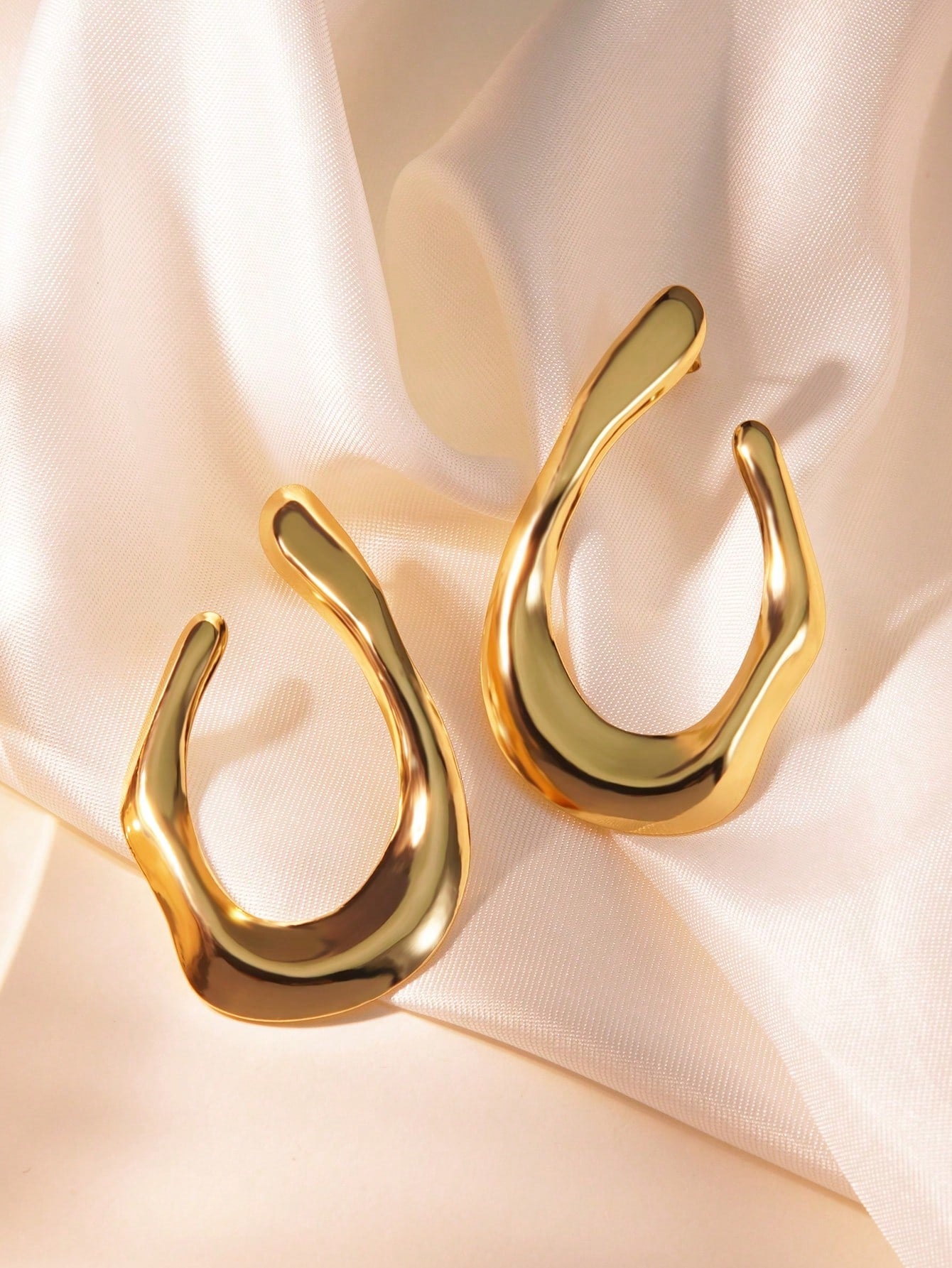 Gold U-shaped earrings on a soft pink fabric background